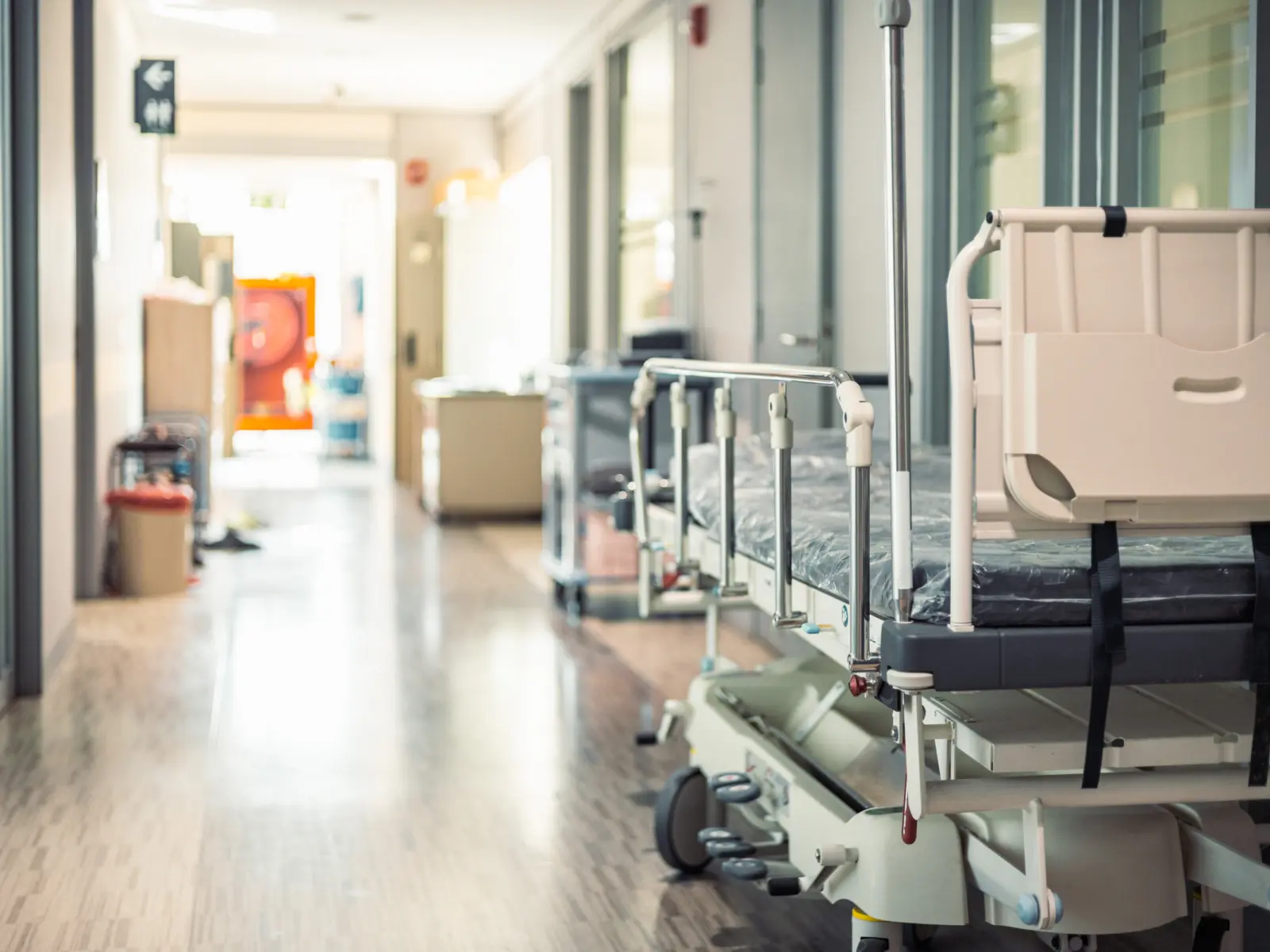 View down a hospital corridor with a hospital bed parked in the hallway.