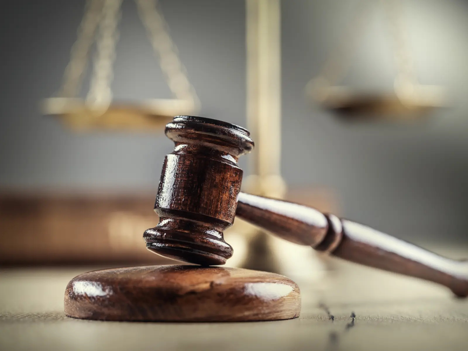 A wooden gavel rests on a circular block, with blurred scales of justice in the background, symbolizing law and order.