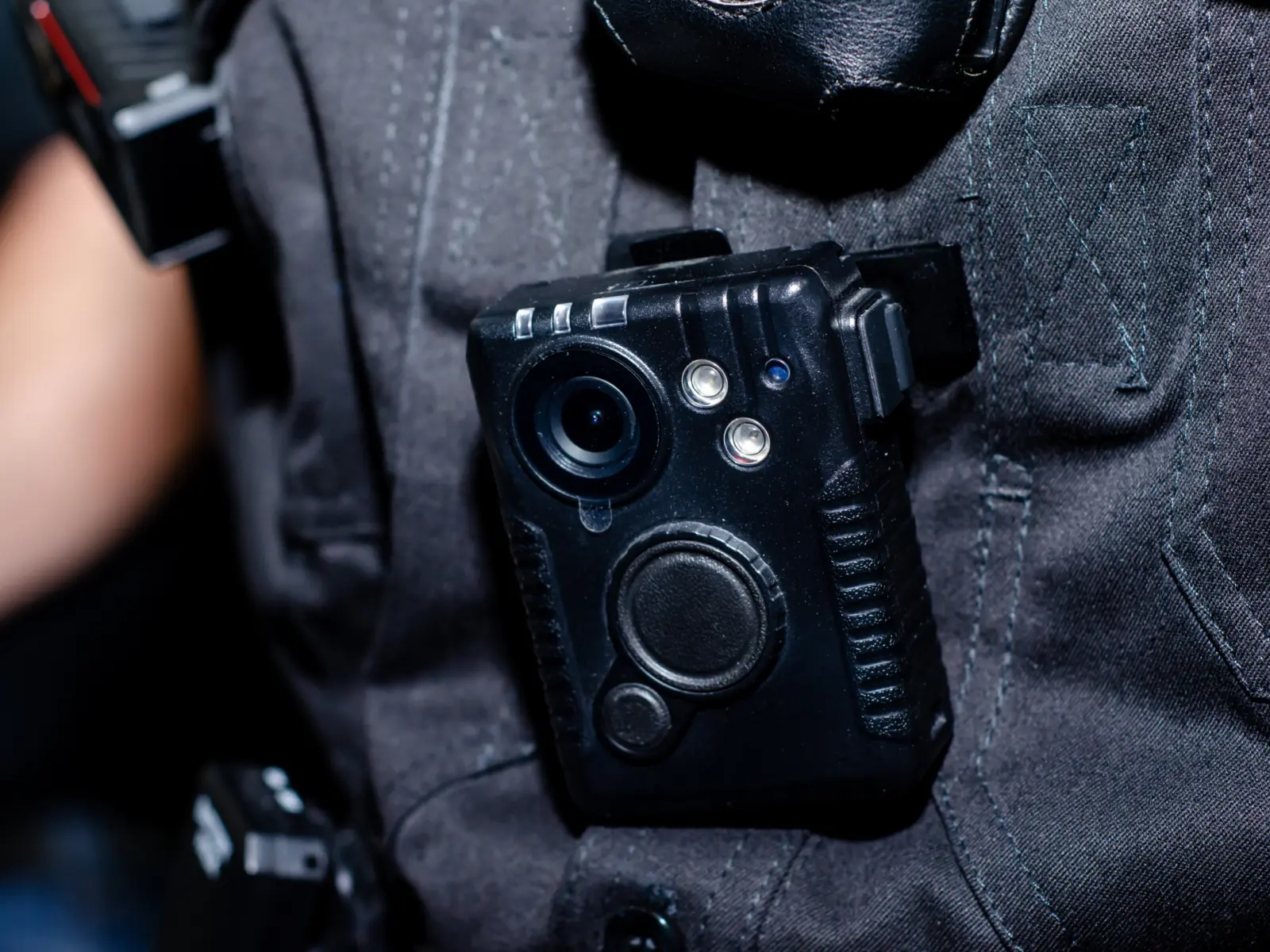 A black body camera is securely attached to a dark uniform, featuring a lens and buttons for operational controls.