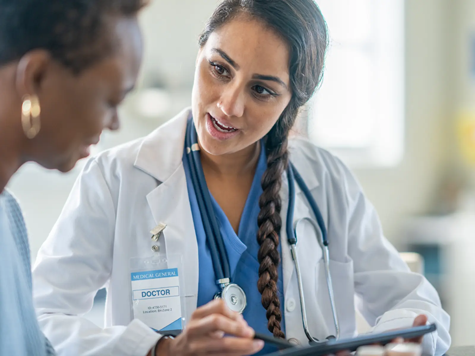 A doctor in a white coat explains information on a tablet to a patient, fostering a focused and empathetic conversation.
