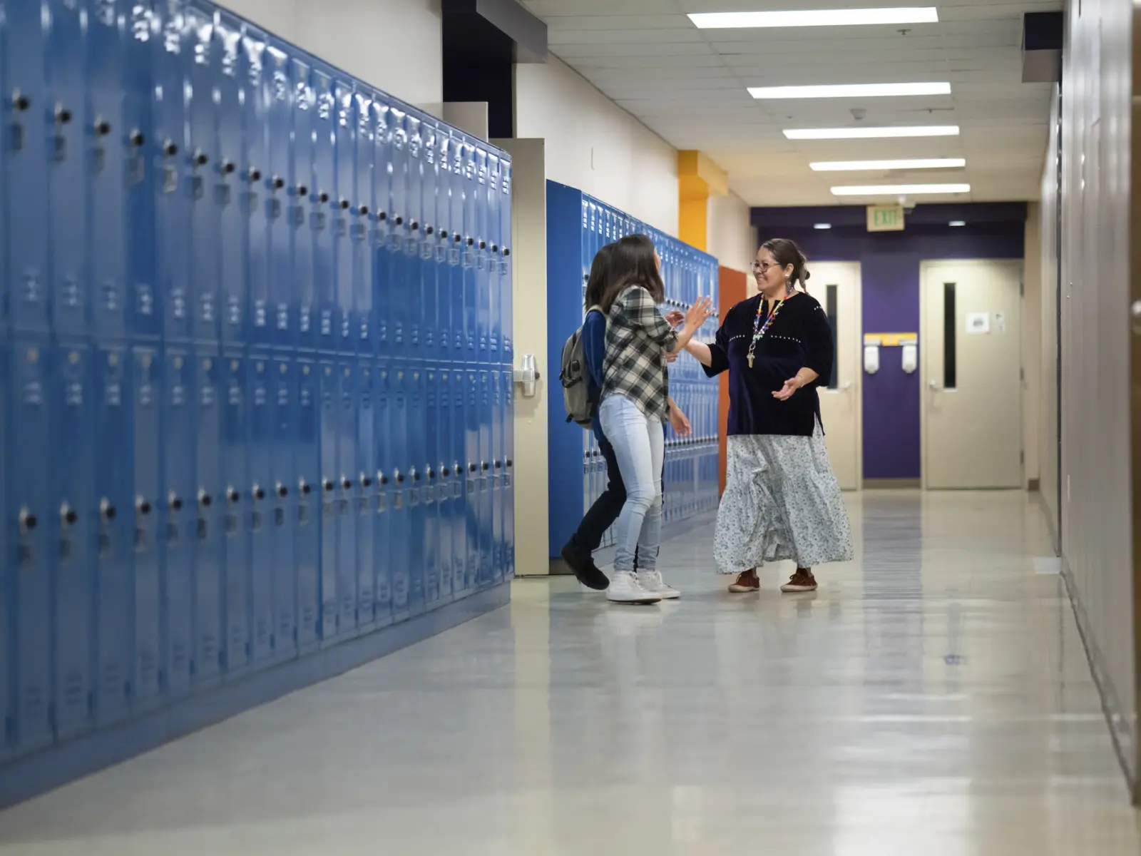 Image of teacher talking with students in hall of school.