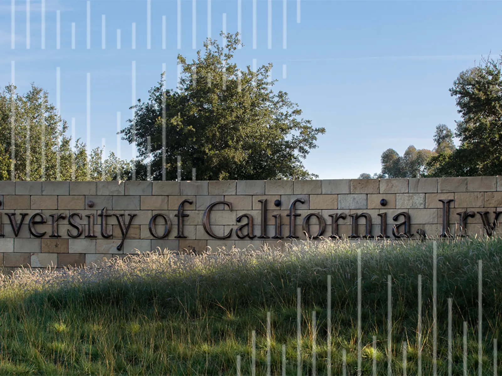 A stone wall features the engraved text "University of California, Irvine," surrounded by greenery and a clear blue sky above.