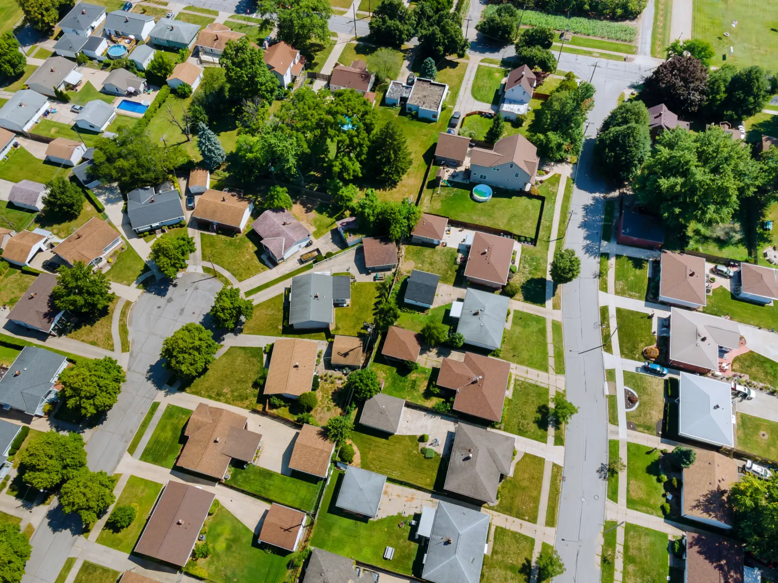 Aerial view of a suburban neighborhood featuring houses with brown roofs, green lawns, and winding streets amidst trees and greenery.