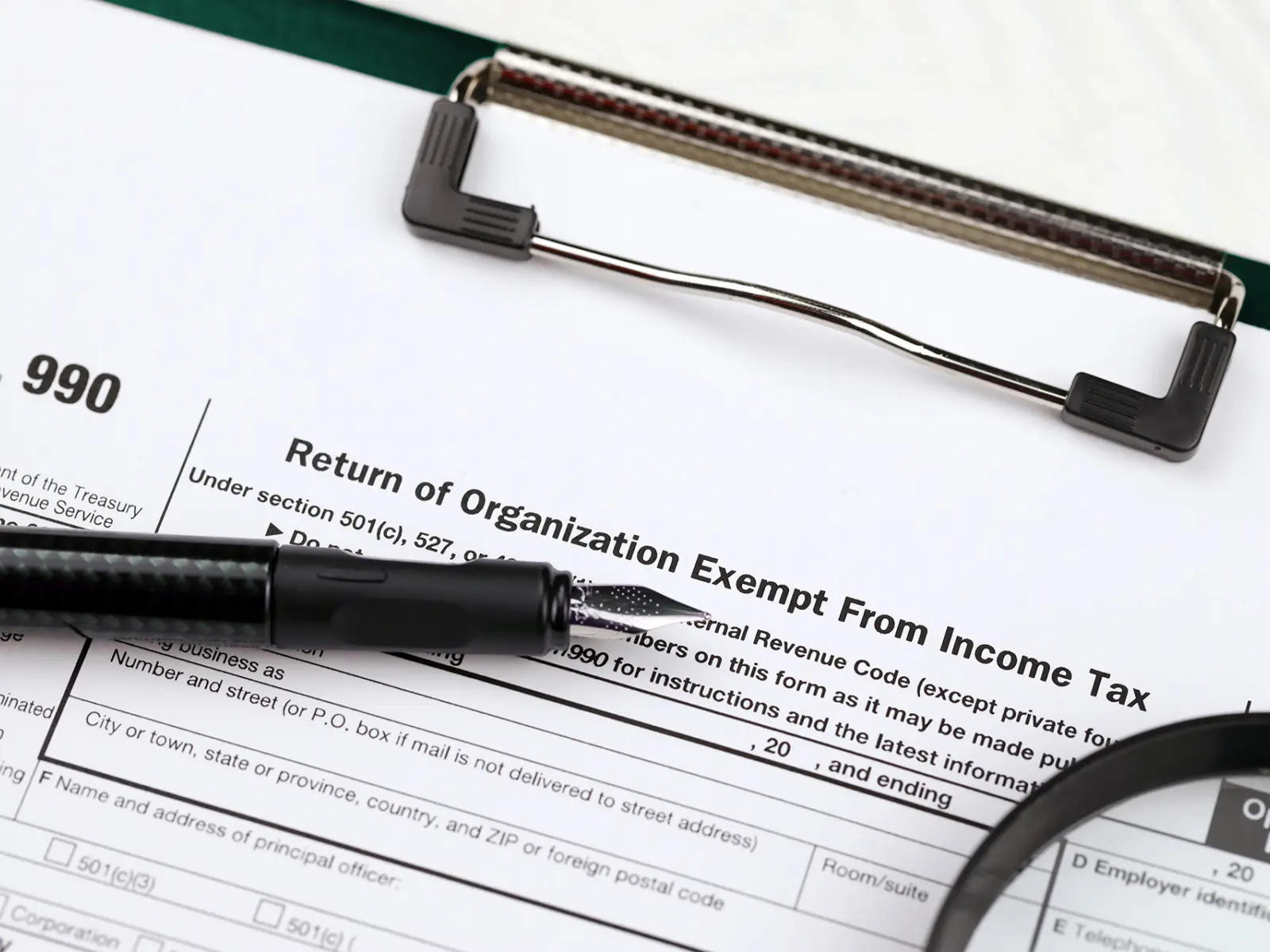 Form 990, titled "Return of Organization Exempt From Income Tax," rests on a table, accompanied by a black pen and a magnifying glass.