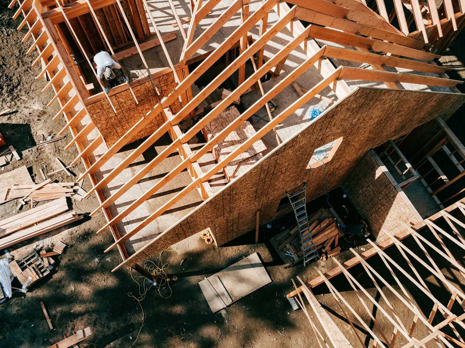 Construction site viewed from above, showcasing wooden framing and workers assembling a structure amid scattered materials and tools.