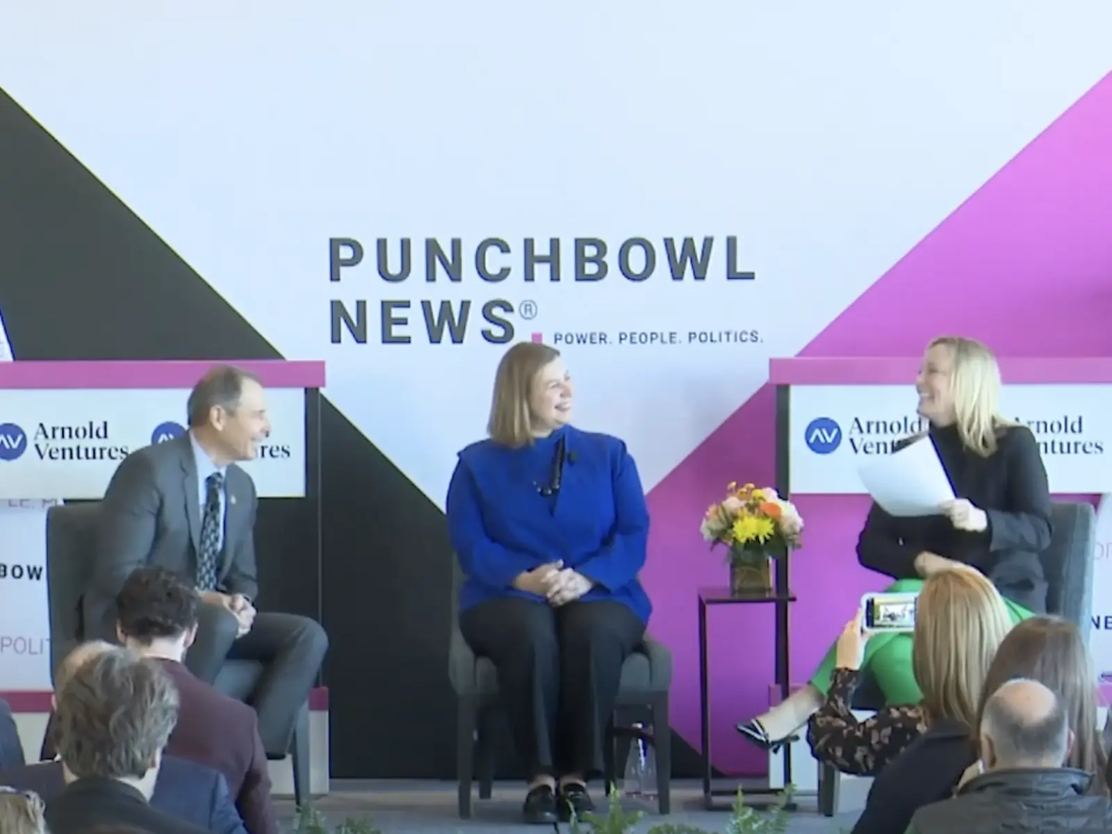 A lively panel discussion at Punchbowl News features three presenters seated on stage, engaging an attentive audience in a modern setting.