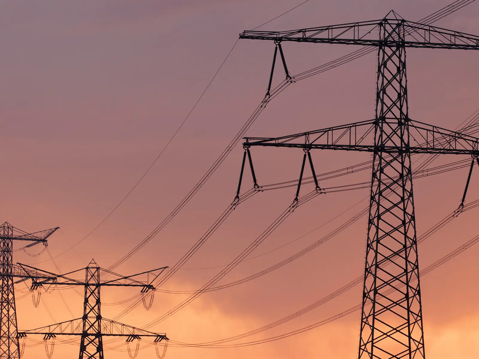 Silhouetted power lines stretch across a colorful sunset, with towers standing tall against a gradient of pink and orange hues.