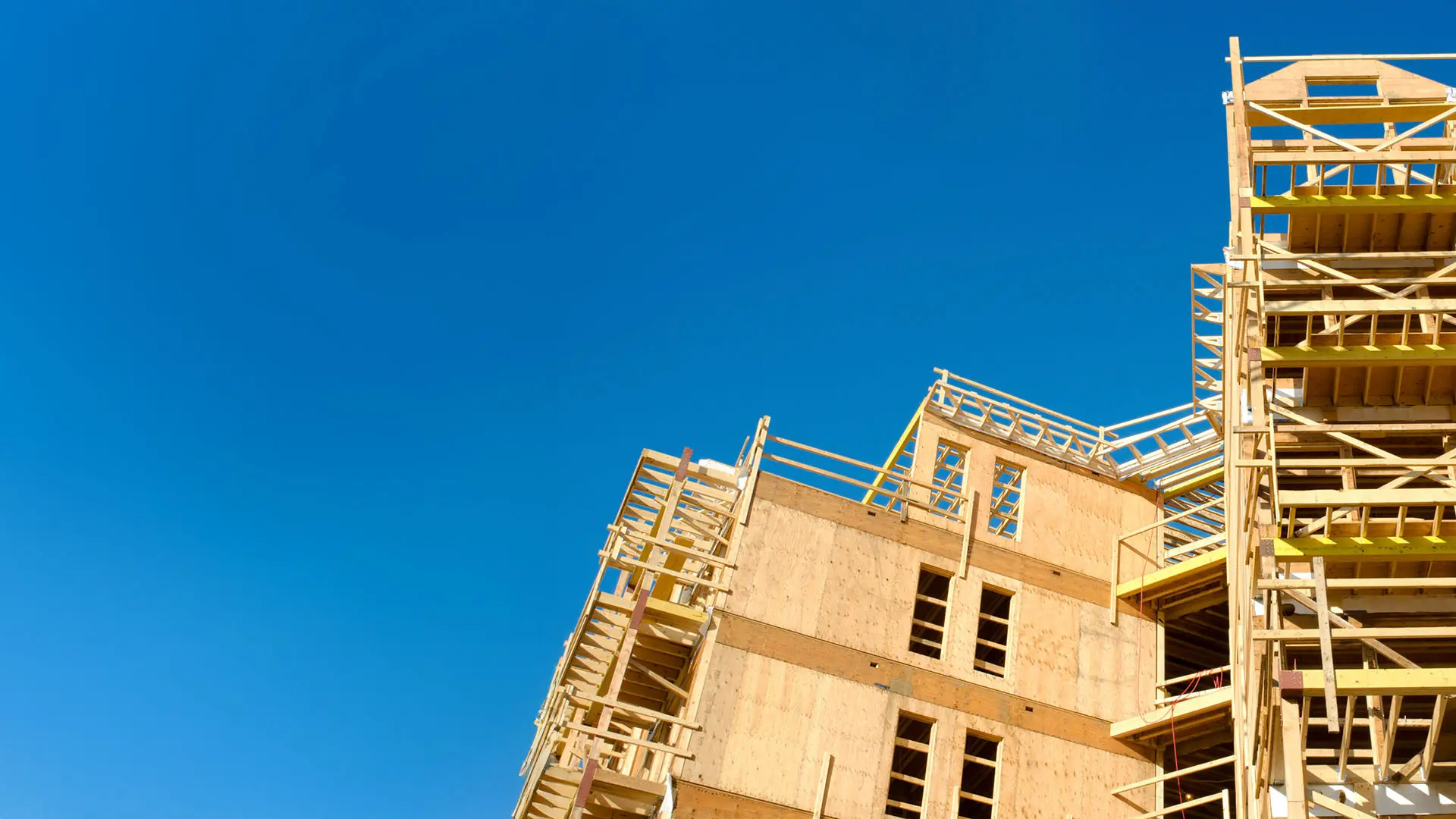 A partially constructed building rises against a clear blue sky, showcasing exposed wooden frames and scaffolding.