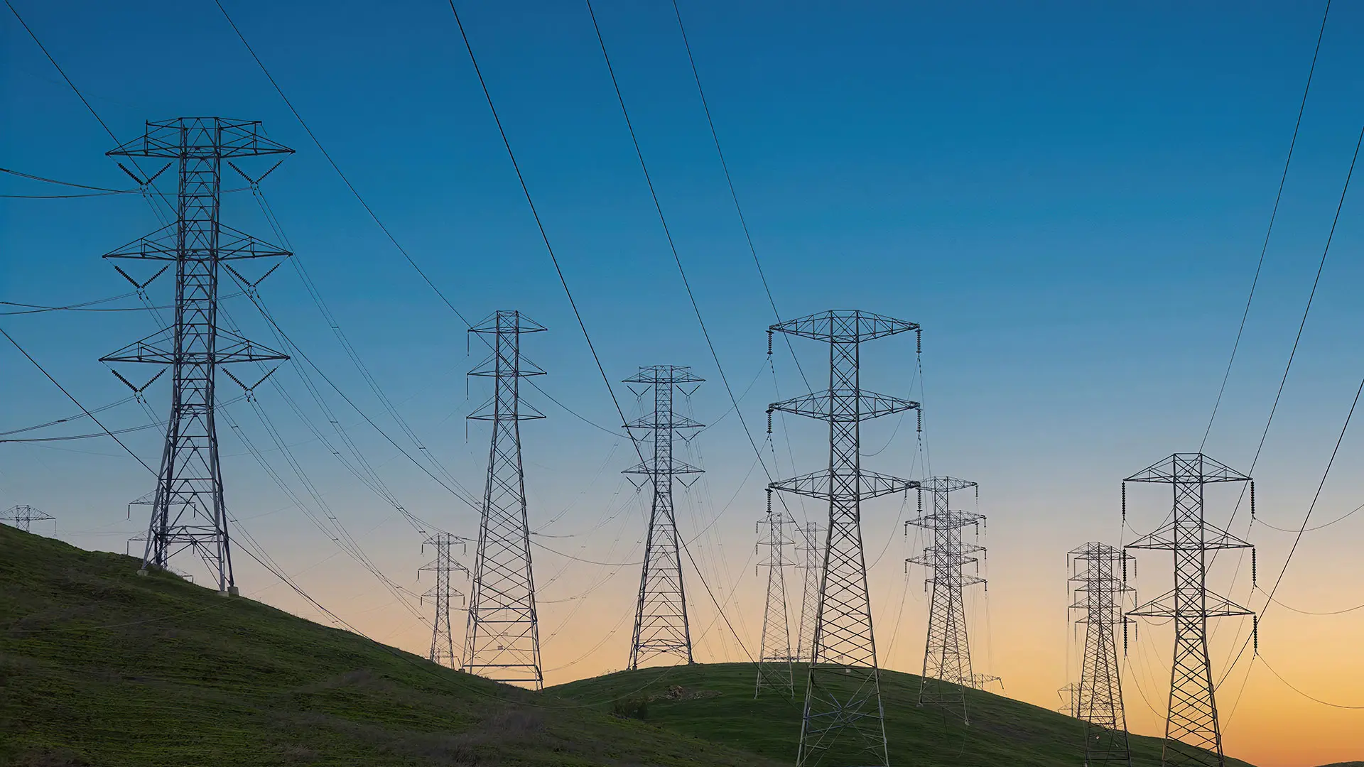 Tall power lines stretch across rolling green hills under a clear blue sky.