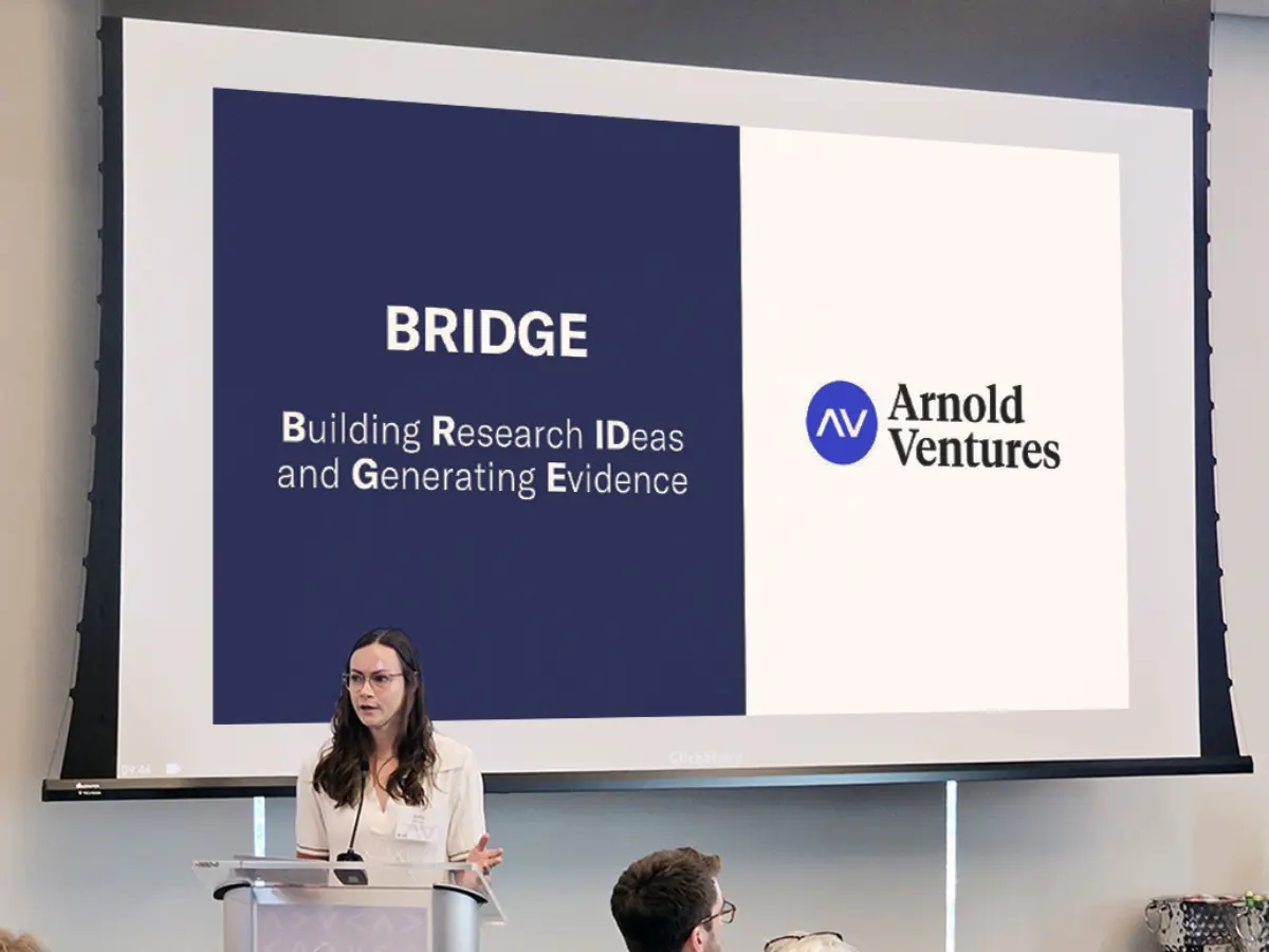 A speaker presents at an AV BRIDGE event, while an engaged audience listens at round tables.