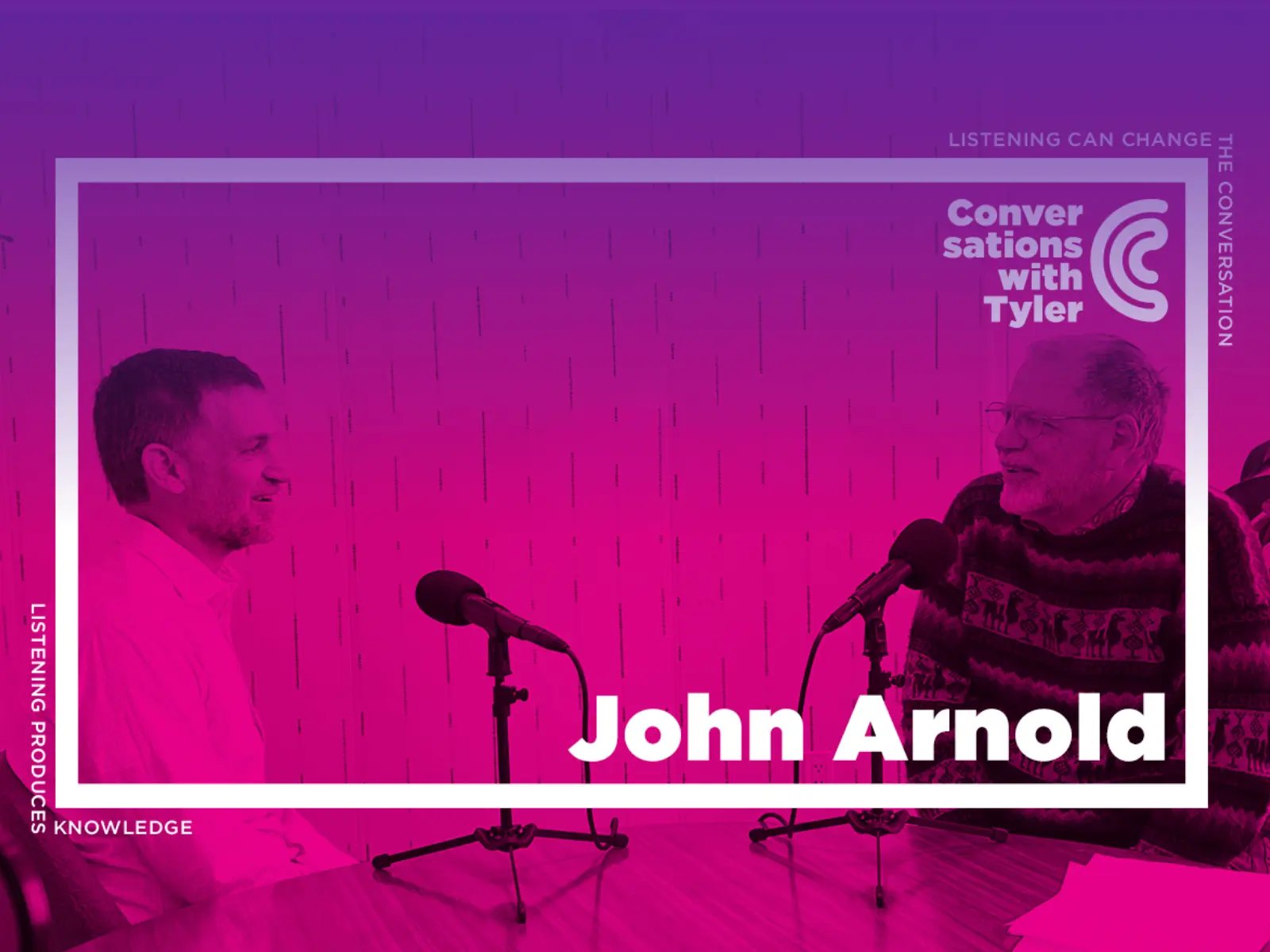 Two men engage in a conversation at a table, microphones in front of them, surrounded by vibrant purple hues and indoor plants.