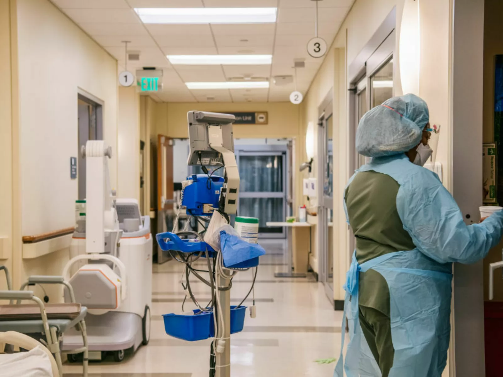 View of hospital corridor with machines and hospital worker in scrubs.