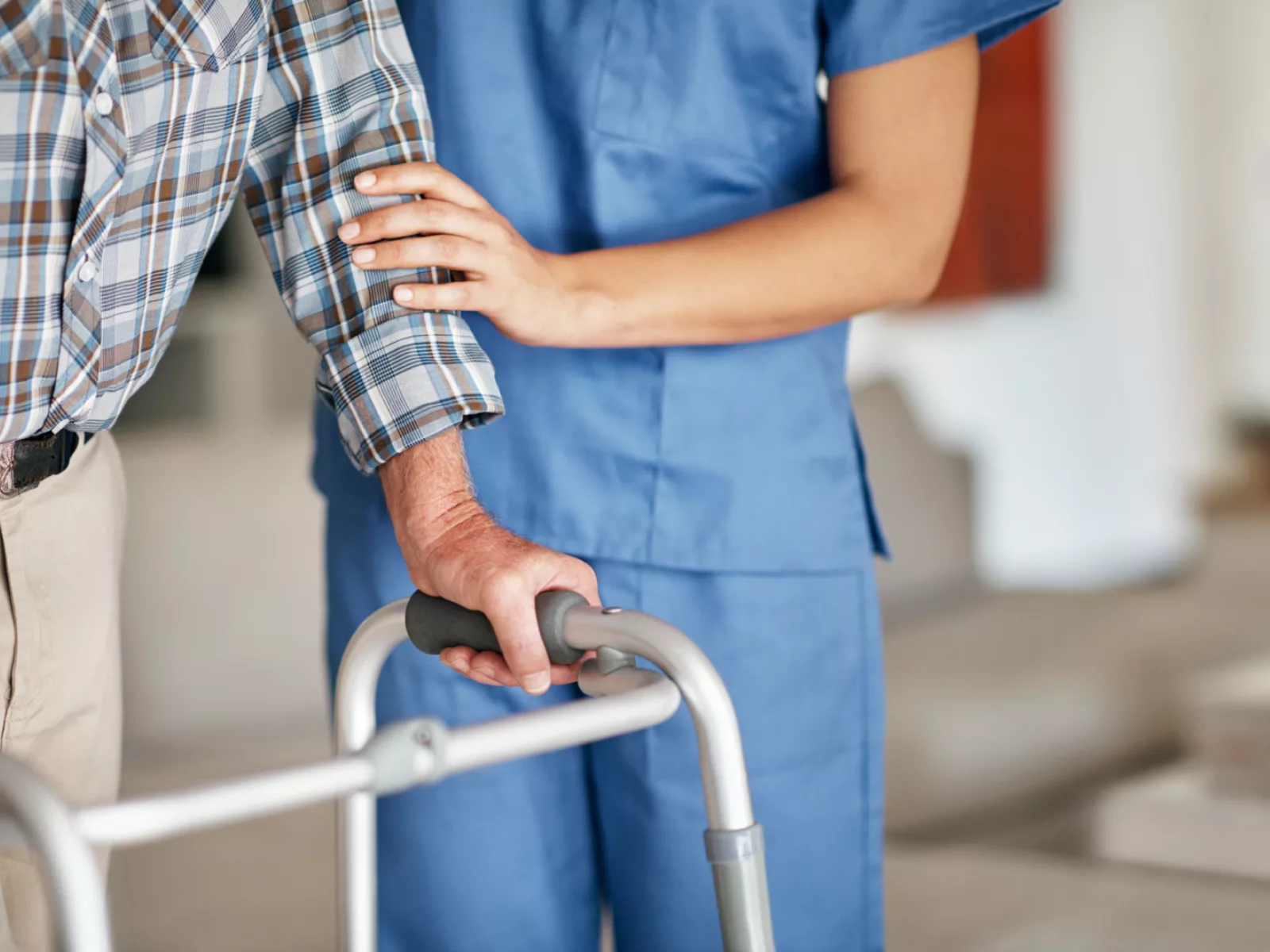 Nurse in scrubs helps guide patient using a walking aid