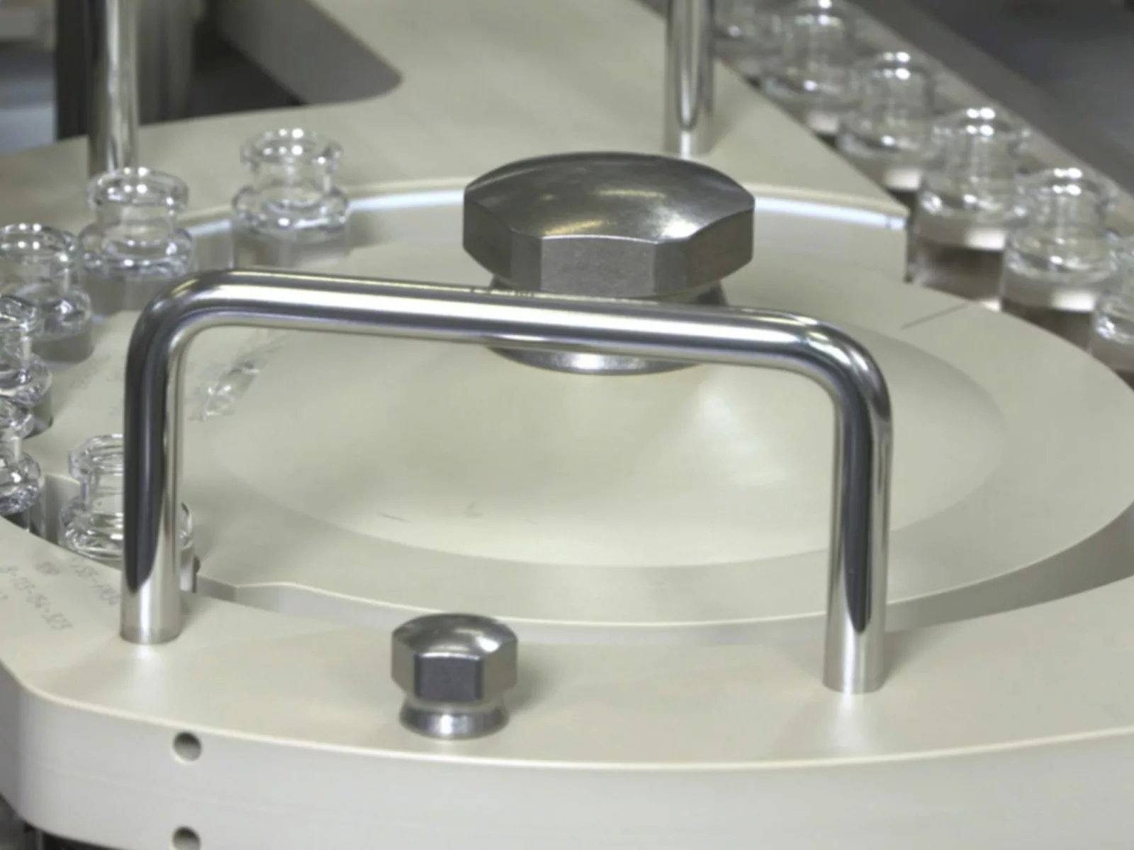 A close-up view of a circular industrial machine component with metallic and beige elements, surrounded by glass vials, showcasing precision engineering.