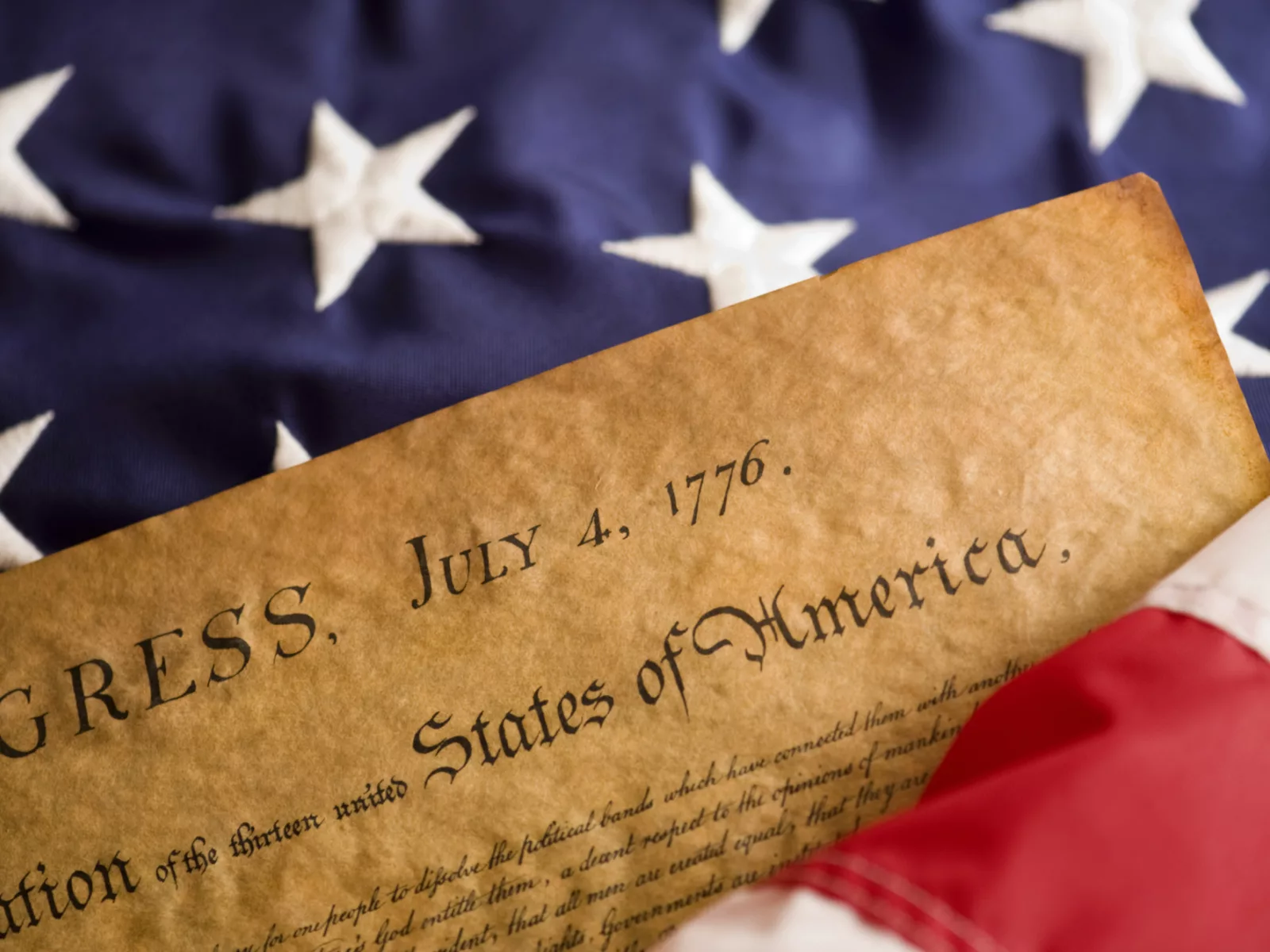 The Declaration of Independence partially rests on a folded American flag, showcasing its historic significance and patriotic colors.