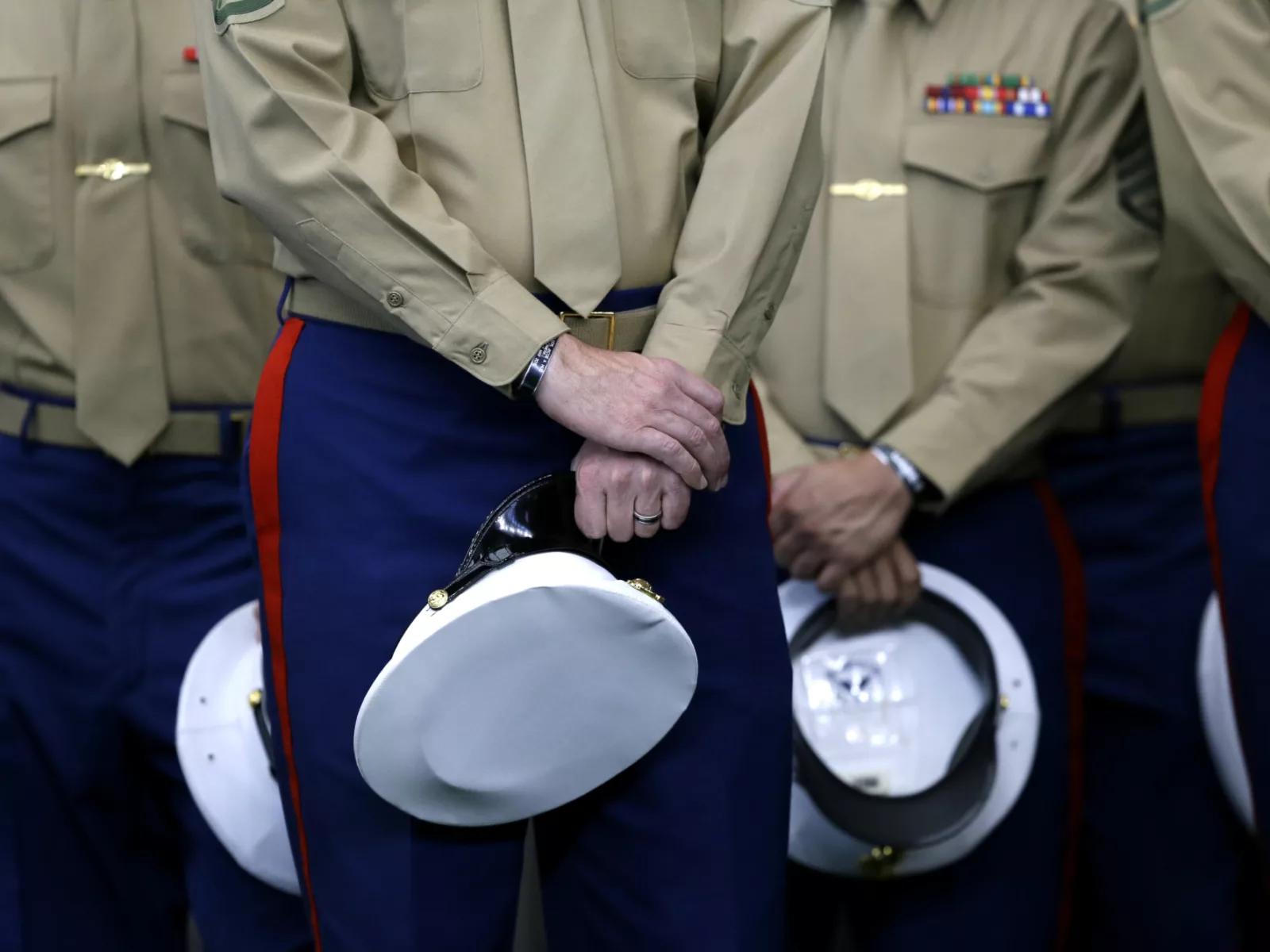Members of a military unit stand in uniform, holding white hats with gold buttons, hands clasped, reflecting discipline and readiness.