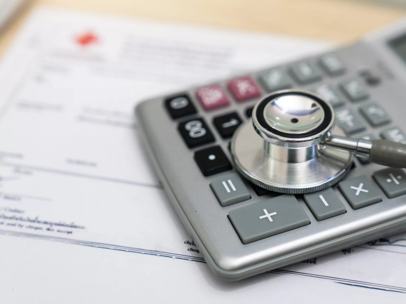 A stethoscope rests on a calculator, set against a background of medical paperwork, symbolizing health and finance.