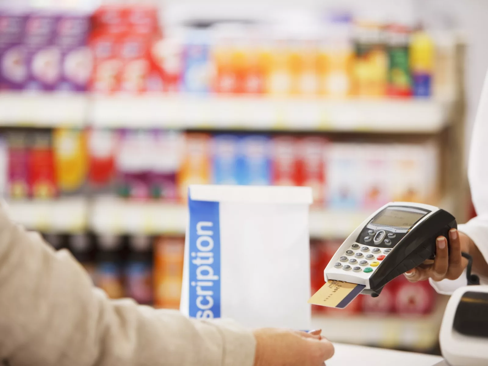 A customer approaches a register, ready to pay with a card at a pharmacy, surrounded by colorful product displays in the background.