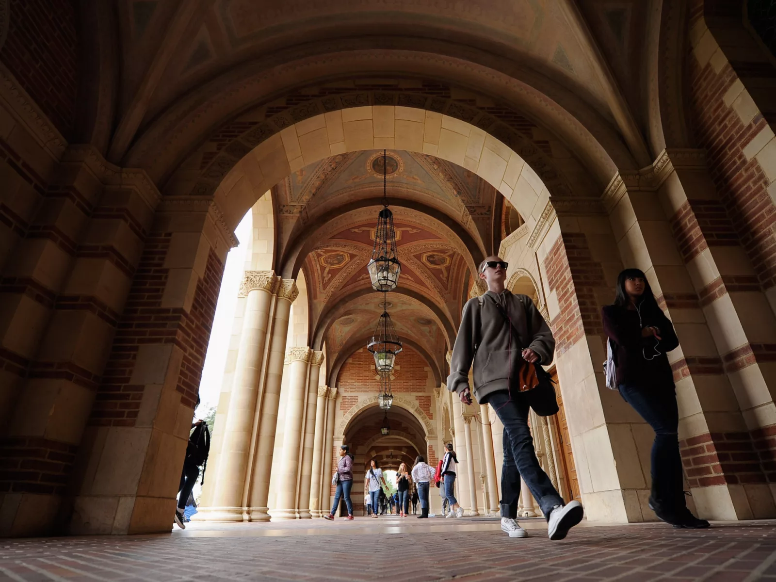 Under arched brick corridors, students walk beneath ornate ceilings and hanging lanterns, creating a vibrant campus atmosphere.